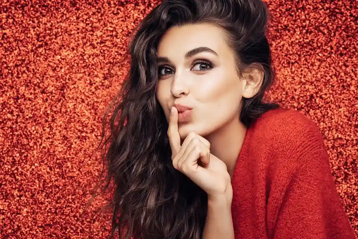 5 HydroGalen akut – meine Geheimwaffe gegen allergische Roetungen Eine weibliche Person vor einem roten Hintergrund hält sich den Zeigefinger in den Lippenbreich