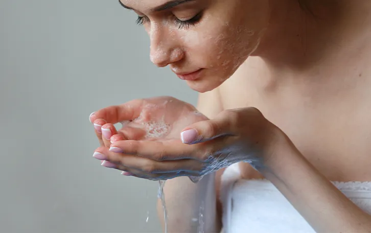 Eine weibliche Person in ein Handtuch eingewickelt hat Seife im Gesicht und seifiges Wasser in den Händen