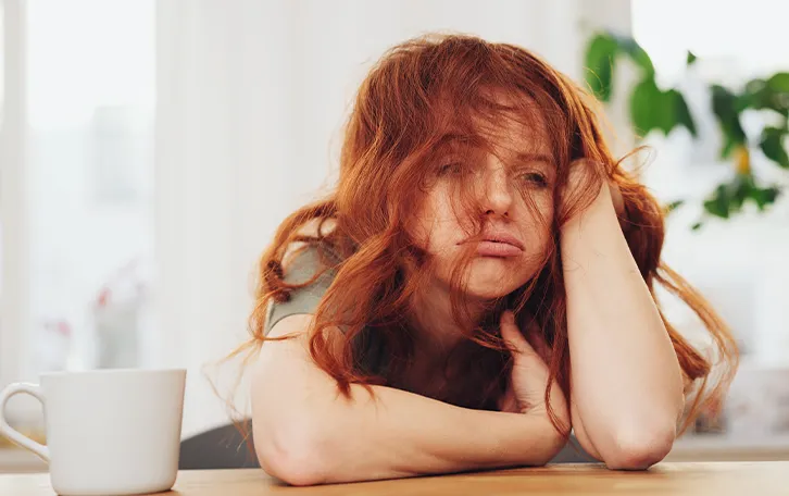 Eine weibliche Person stützt den Kopf auf einen Arm und sieht gestresst aus
