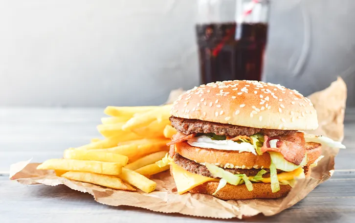 Ein Hamburger mit Pommes Frites und einem Glas Cola im Hintergrund