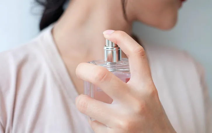 Eine weibliche Person sprüht sich ein Parfum auf den Halsbereich