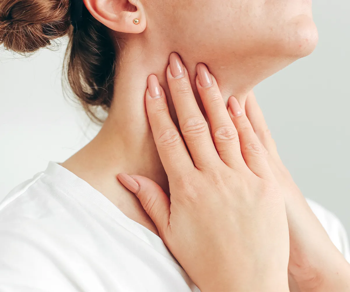 Eine weibliche Person greift sich mit beiden Händen an den Hals