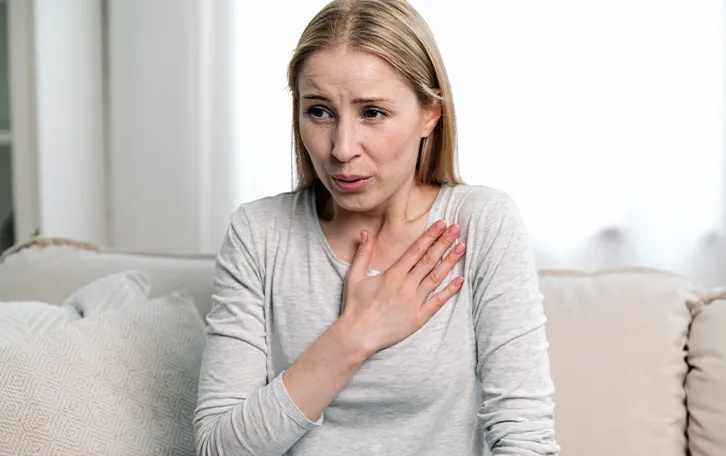 Eine Frau hält sich eine Hand an die Brust und spitzt die Lippen, als würde sie schwer Luft bekommen