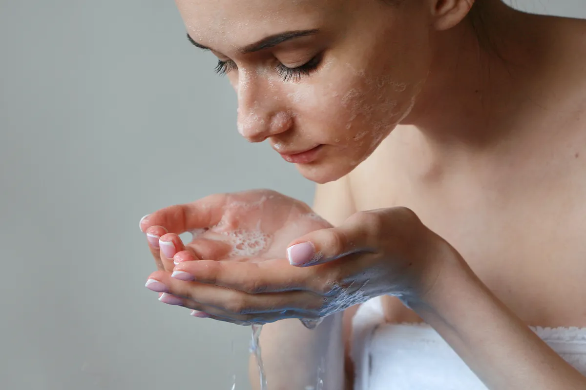 Richtige Pflege bei Hautausschlag Eine weibliche Person in ein Handtuch eingewickelt hat Seife im Gesicht und seifiges Wasser in den Händen