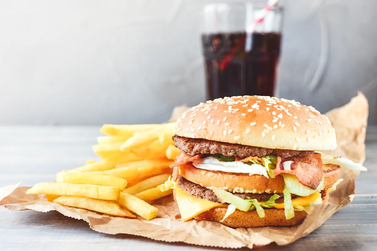 Ein Hamburger mit Pommes Frites und einem Glas Cola im Hintergrund