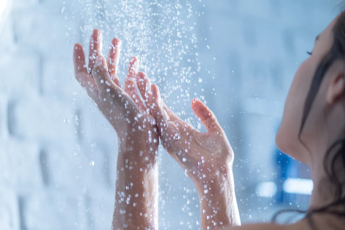 Eine weibliche Person hält die Hände unter das fließende Wasser einer Dusche